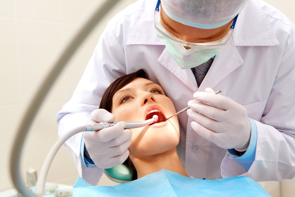 Photo of female patient with dentist over her checking up teeth and drilling them